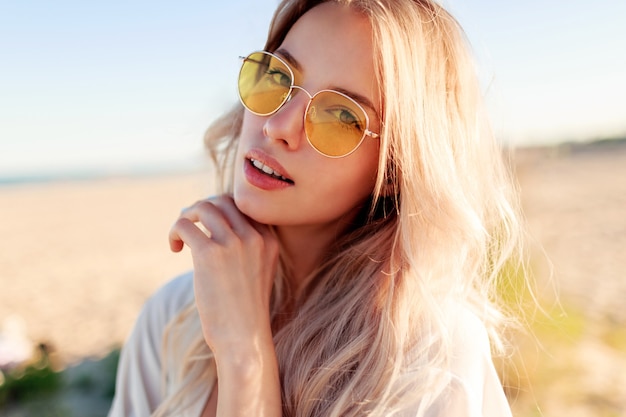 Cerrar retrato de niña rubia sonriente juguetona jugando con pelos, divirtiéndose y disfrutando del verano en la playa.