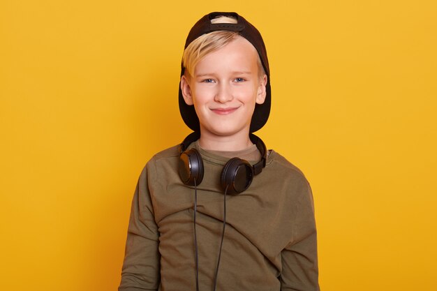 Cerrar retrato de niño rubio con ropa casual, gorra, mantiene los auriculares alrededor del cuello