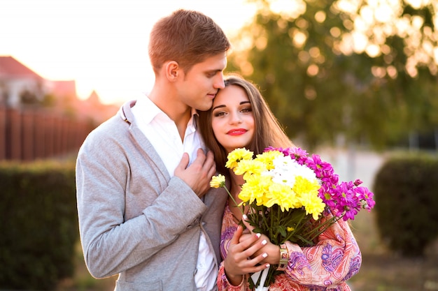 Cerrar un retrato de una pareja increíble en el amor, abrazos en la calle, estilo elegante, estado de ánimo vintage, amor, emociones, hombre guapo y mujer impresionante, cita romántica, presente ramo de flores.