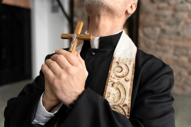Cerrar sacerdote orando con crucifijo
