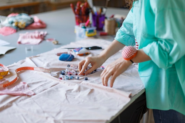 Foto gratuita cerrar sastre en camisa eligiendo hilo colorido mientras trabaja con tela en un taller de costura moderno