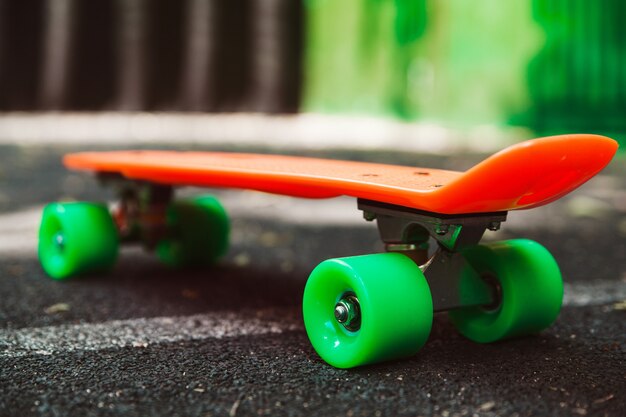 Cerrar skateboard penny naranja sobre asfalto detrás de la pared verde
