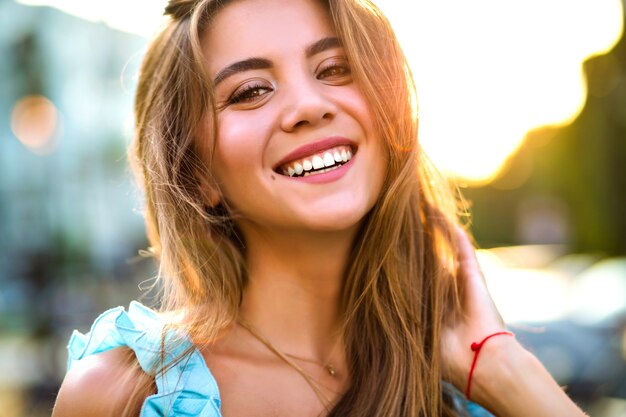 Cerrar soleado retrato de hermosa mujer magnífica con maquillaje natural y gran sonrisa asombrosa mirando a cámara, luz solar brillante, estado de ánimo positivo.