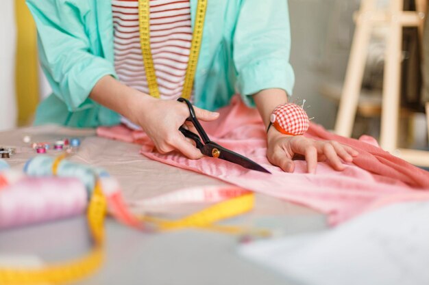 Cerrar tela de corte de costurera con tijeras en taller de costura moderno