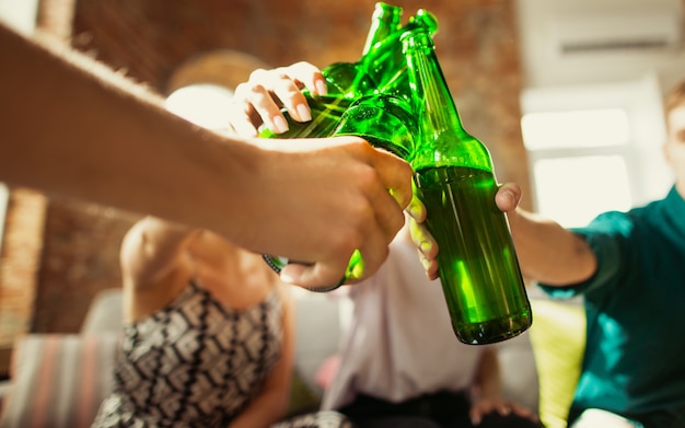 Cerrar tintineo. Joven grupo de amigos bebiendo cerveza, divirtiéndose, riendo y celebrando juntos.