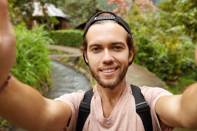 Cerrar vista de cara feliz de excursionista atractivo con barba sonriendo mientras toma selfie