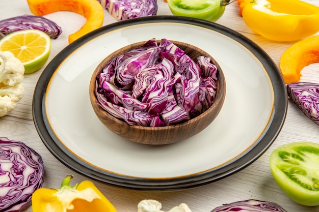 Cerrar vista inferior cortar las coles rojas en un tazón en un plato redondo cortar verduras en la superficie blanca