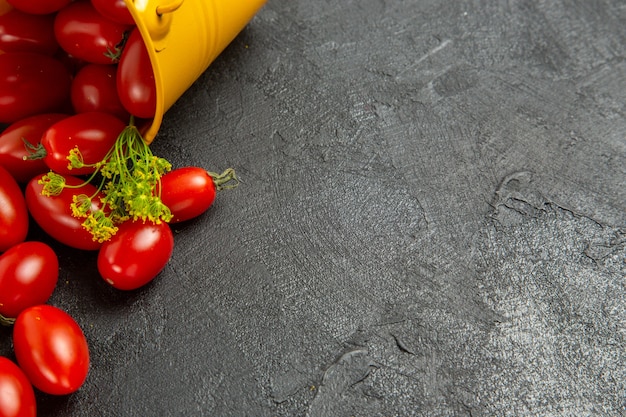 Cerrar vista inferior cubo amarillo volcado lleno de tomates cherry y flores de eneldo en la parte superior izquierda del fondo oscuro