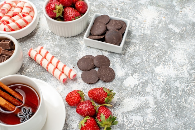 Foto gratuita cerrar vista inferior cuencos con fresas, chocolates, caramelos y té de semillas de anís y canela en el lado izquierdo del fondo blanco grisáceo