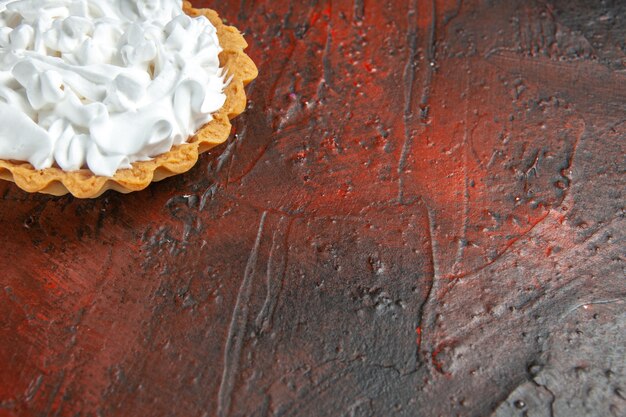 Cerrar vista inferior pequeña tarta con crema pastelera en el espacio de copia de mesa rojo oscuro