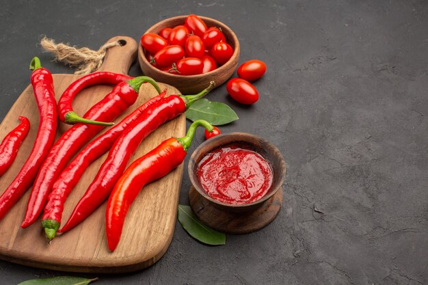 Cerrar vista inferior un plato de tomates cherry pimientos rojos en la tabla de cortar hojas de laurel y un plato de salsa de tomate en la mesa negra