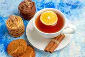 Foto gratuita cerrar vista inferior taza de té con sabor a limón y galletas de canela atadas con una cuerda en el cuadro azul