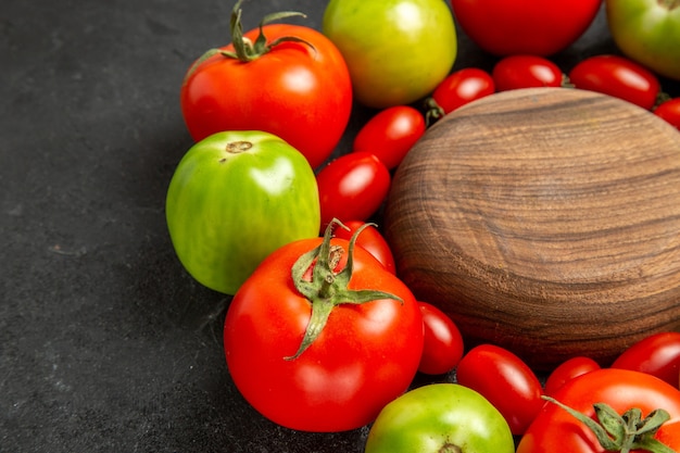 Cerrar vista inferior tomates rojos y verdes cereza alrededor de una placa de madera sobre fondo oscuro