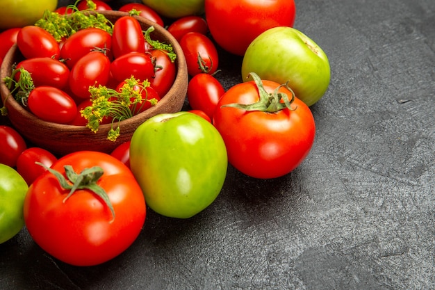 Cerrar vista inferior tomates rojos y verdes cereza alrededor de un recipiente con tomates cherry y flores de eneldo sobre fondo oscuro