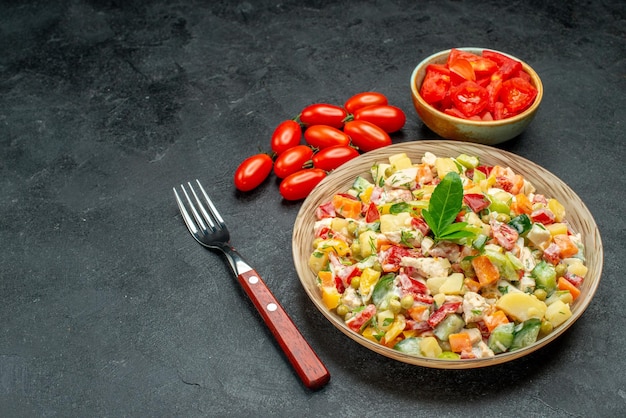 Cerrar vista lateral de ensalada de verduras con tomates y tenedor sobre fondo gris oscuro