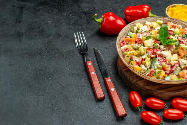 Cerrar vista lateral de ensalada de verduras con verduras y cubiertos sobre fondo gris oscuro