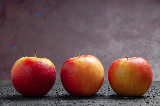 Cerrar vista lateral frutas tres manzanas de color amarillo rojizo sobre una mesa de madera gris sobre un fondo púrpura