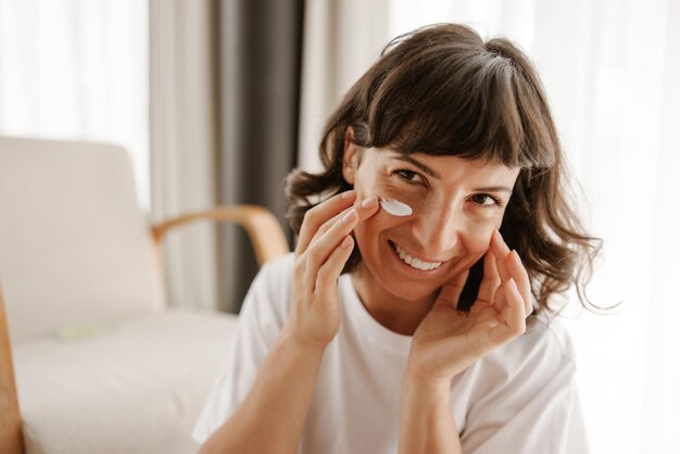 Cerrar vista de mujer sonriente para crema para la piel mirando a la cámara