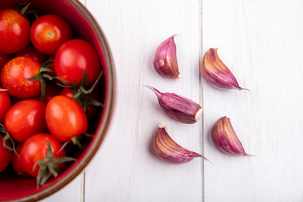 Foto gratuita cerrar vista de verduras como tomates en un tazón y dientes de ajo en la pared de madera