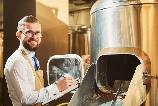 Cervecero masculino alegre mirando a la cámara mientras escribe datos