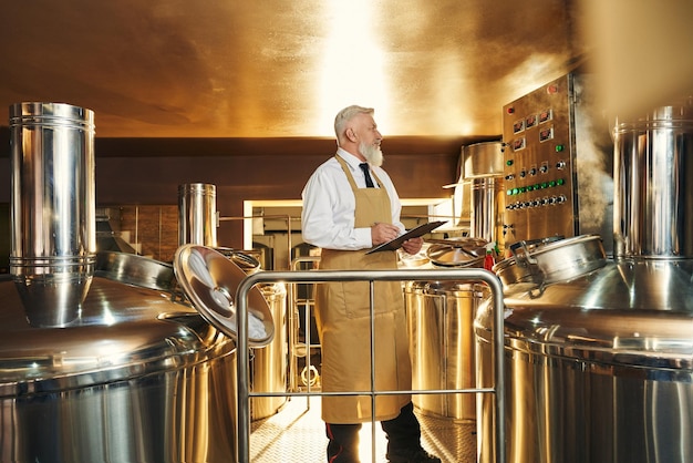 Foto gratuita cervecero masculino manteniendo la carpeta y controlando la producción de cerveza