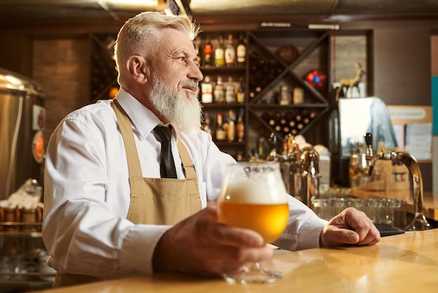 Cervecero masculino profesional de pie sobre el bar y bebiendo cerveza