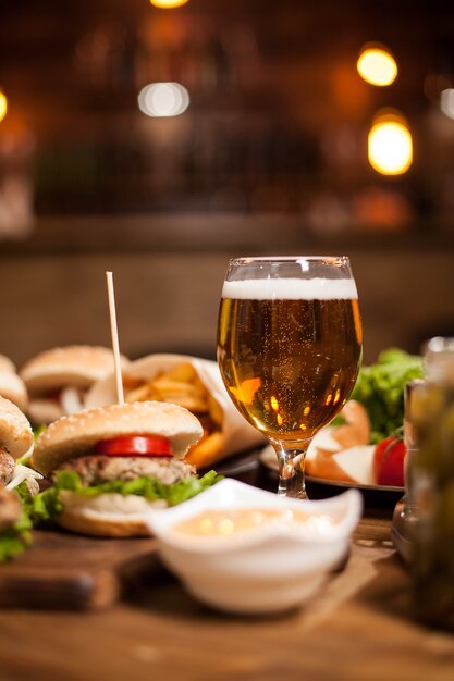 Cerveza dorada junto a deliciosas hamburguesas en mesa de madera. Papas fritas. Ensalada verde. Papas fritas. Salsa de Ajo.