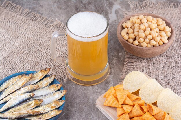 Cerveza espumosa y surtido de snacks sobre superficie de mármol. Foto de alta calidad