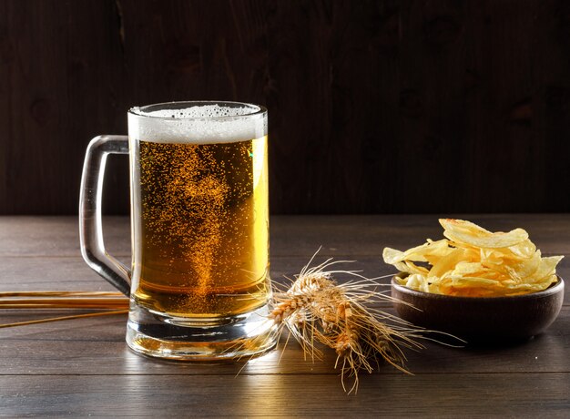 Cerveza en un vaso con espigas, vista lateral de chips en una mesa de madera