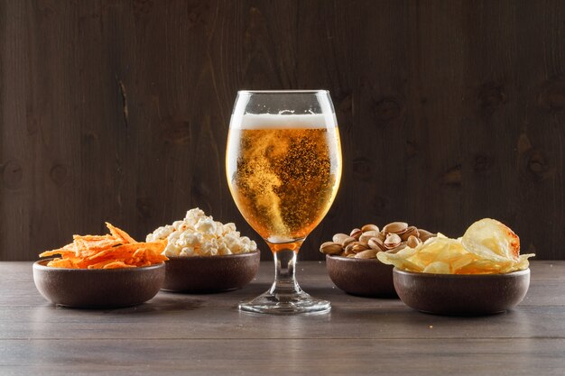 Cerveza en un vaso con vista lateral de comida chatarra en una mesa de madera