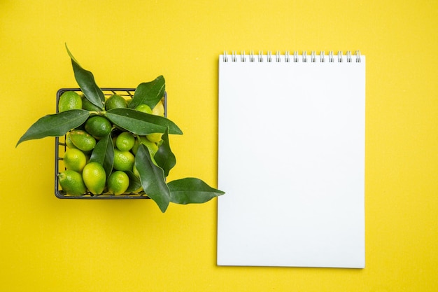 Cesta de frutas cítricas de vista superior de frutas cítricas verdes con hojas cuaderno blanco