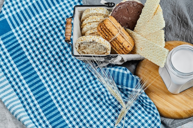 Cesta de galletas y un tarro de leche sobre una mesa de mármol con un mantel.