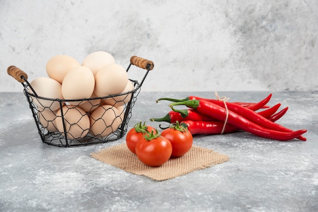 Cesta de huevos crudos frescos, chiles y tomates en mármol.