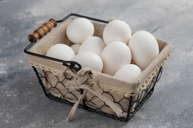 Cesta llena de huevos de gallina blancos frescos en un mármol.