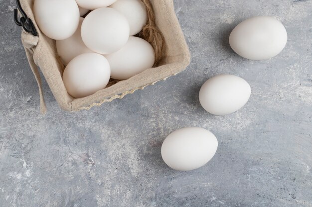 Cesta llena de huevos de gallina blancos frescos en un mármol.