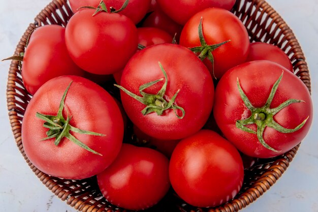 Cesta llena de tomates en superficie blanca