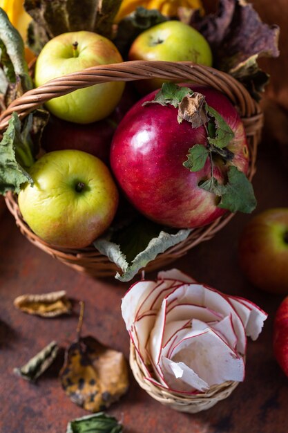 Cesta de manzanas, manzanas secas, calabacín y hojas de otoño sobre una mesa marrón oxidada