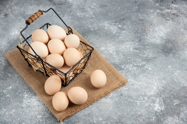 Cesta metálica de huevos de gallina cruda sobre superficie de mármol.