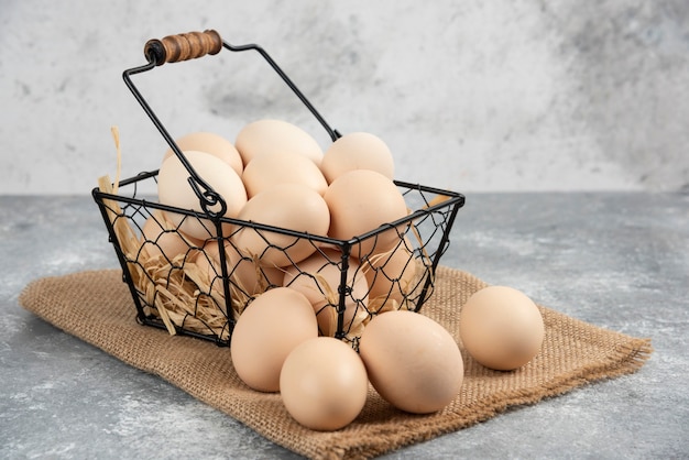 Foto gratuita cesta metálica de huevos de gallina cruda sobre superficie de mármol.