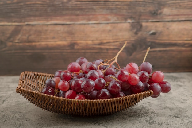 Cesta de mimbre de deliciosas uvas rojas sobre mesa de mármol.