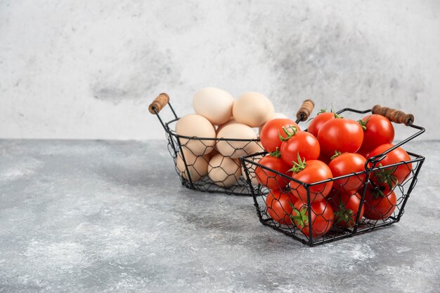 Cesta de mimbre de huevos orgánicos crudos y tomates rojos sobre mármol.