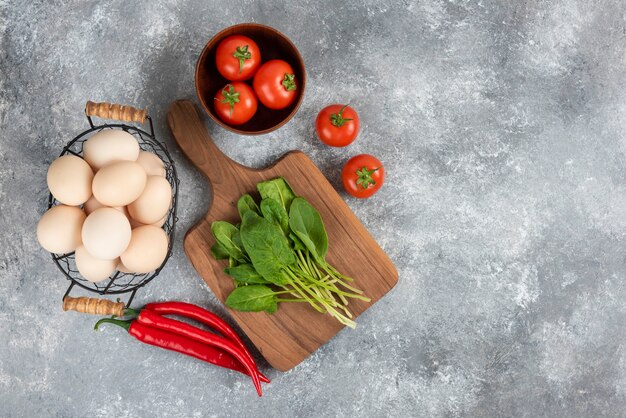 Cesta de mimbre de huevos orgánicos crudos y verduras frescas en mármol.