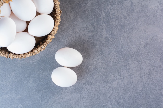 Cesta de mimbre llena de huevos orgánicos en la mesa de piedra.