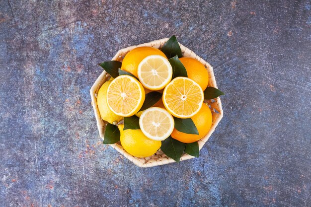 Cesta de mimbre llena de limones frescos con hojas de mármol.