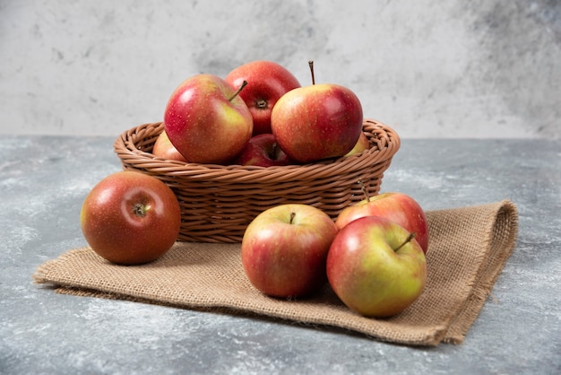 Cesta de mimbre de manzanas maduras brillantes sobre superficie de mármol.