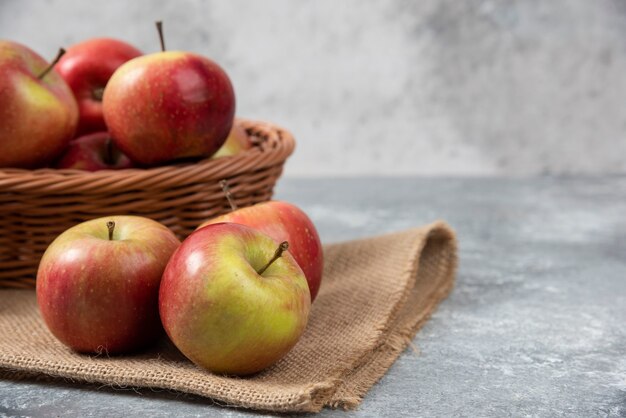 Cesta de mimbre de manzanas maduras brillantes sobre superficie de mármol.