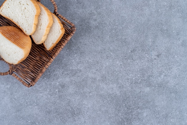 Cesta de mimbre de pan blanco en rodajas colocado sobre la mesa de piedra.