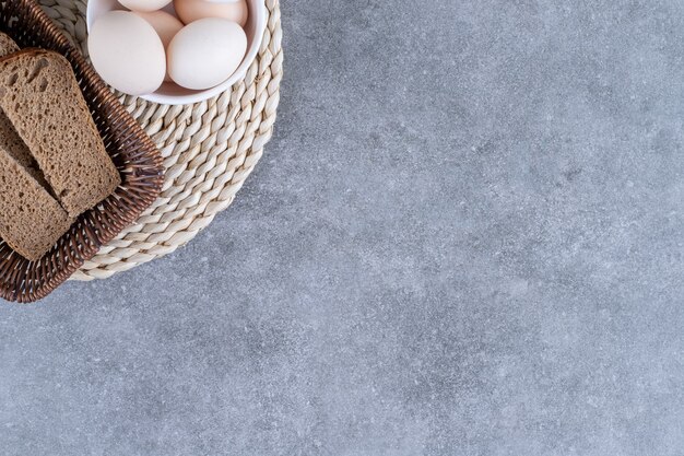 Cesta de mimbre de pan de centeno y cuenco de huevos crudos en la mesa de piedra.