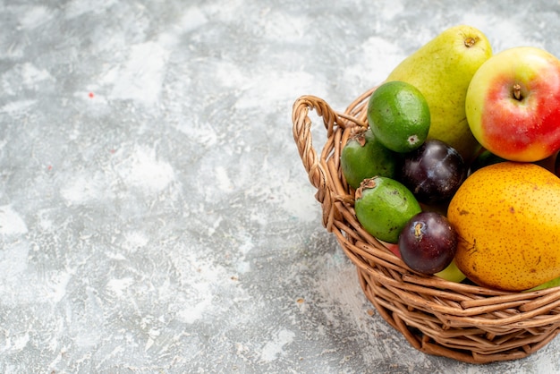 Cesta de mimbre de plástico con media vista superior con peras de manzana, ciruelas feykhoas y caqui a la derecha de la mesa gris