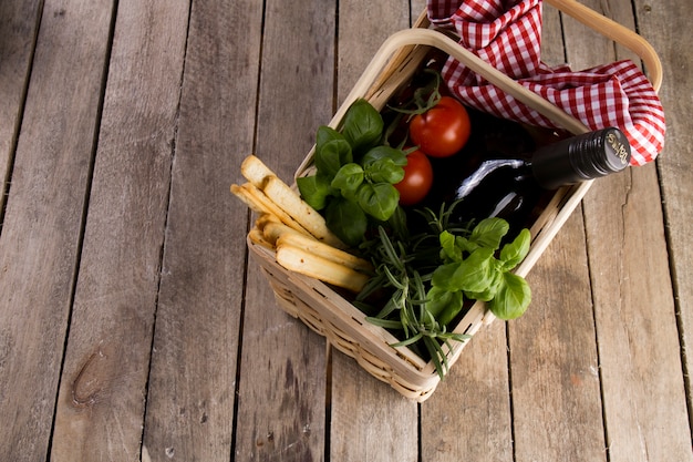 Cesta de mimbre con tomates, botella y hierbas aromáticas